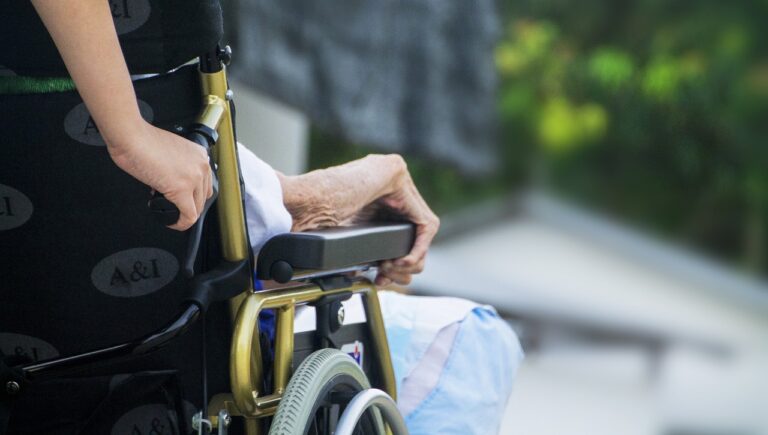 Partial view of an old person being pushed in a wheelchair